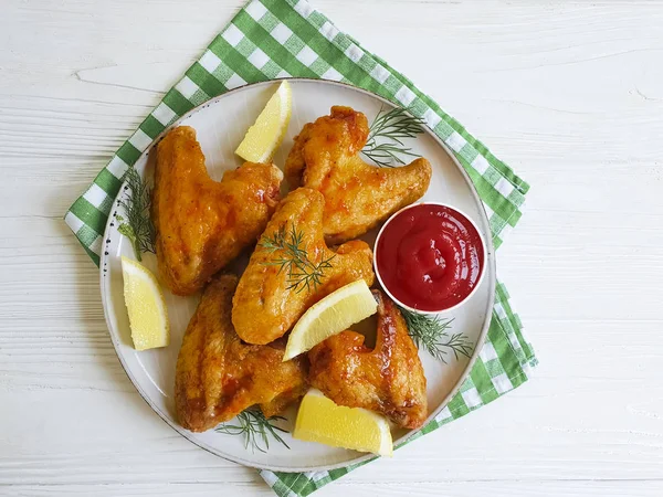 fried wings, ketchup, lemon on a wooden background