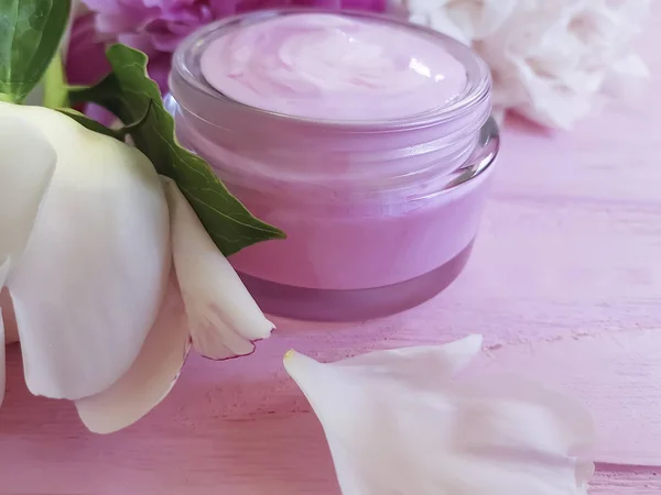 cream cosmetic, peony flower on a pink wooden background