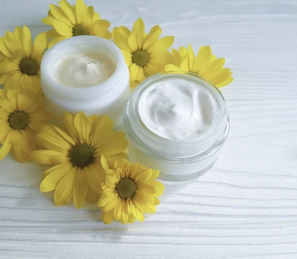 cream cosmetic yellow daisy flowers on a white wooden background