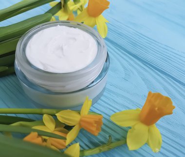 mavi ahşap arka plan üzerinde kozmetik krem nergis çiçek