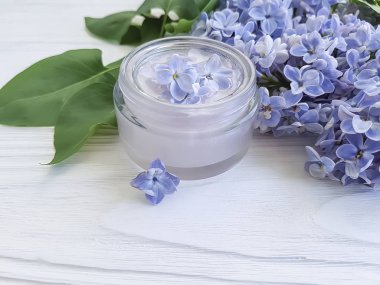cosmetic cream, lilac flower on a white wooden background clipart