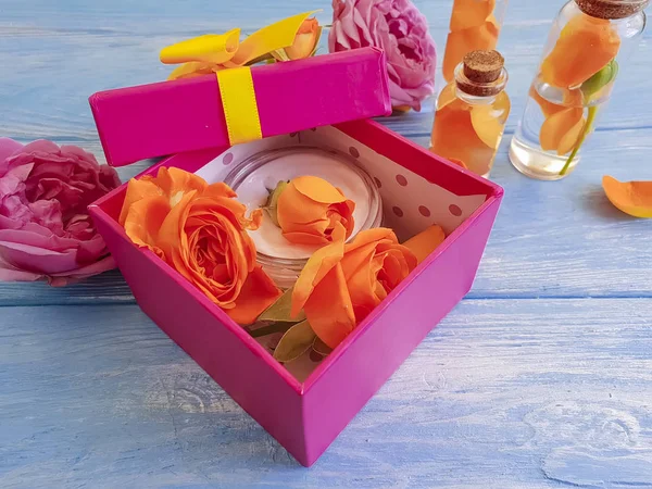 extract, essence gift box cosmetic cream fresh orange rose on a blue wooden background