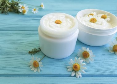 mavi ahşap arka plan üzerinde kozmetik krem çiçek papatya