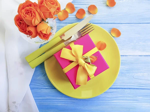 plate, gift box, flower rose on a blue wooden background