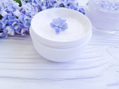 Beyaz ahşap zemin üzerinde kozmetik krem, çiçek leylak