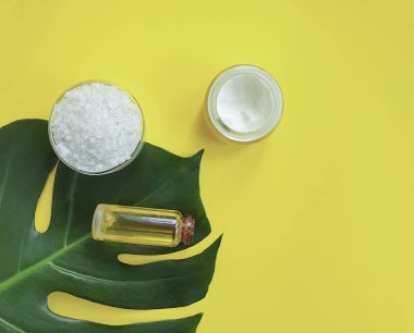 Sarı bir arka plan üzerinde kozmetik krem, monstera yaprak