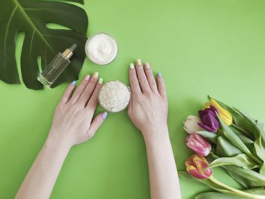 kadın elleri manikür, kozmetik krem, renkli bir arka plan üzerinde lale çiçeği