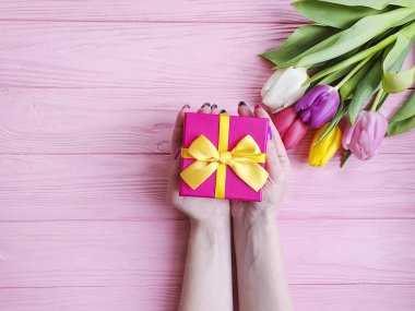 women's hands hold a gift box, a bouquet of tulips on a pink wooden background