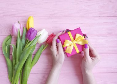 women's hands hold a gift box, a bouquet of tulips on a pink wooden background