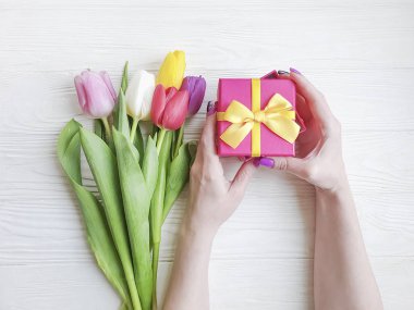 Kadınların elinde bir hediye kutusu, ahşap bir arka planda bir buket lale.