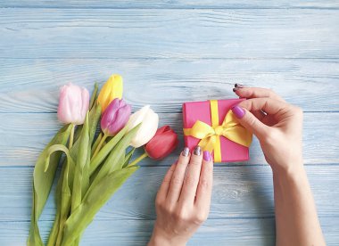 Kadınların elinde bir hediye kutusu, ahşap bir arka planda bir buket lale.