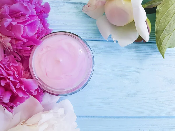 cosmetic cream, peony flower on a blue wooden background