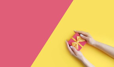 Kadın elleri renkli bir arka planda hediye kutusunu tutuyor.