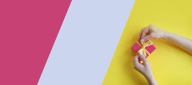 Kadın elleri renkli bir arka planda hediye kutusunu tutuyor.