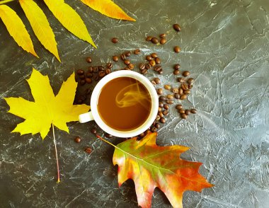 Bir fincan kahve, arka planda sonbahar yaprakları.
