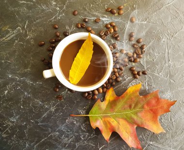 Bir fincan kahve, arka planda sonbahar yaprakları.