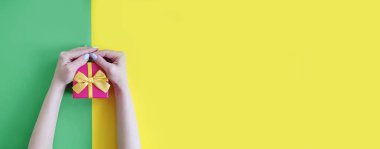 Renkli bir arka planda hediye kutusu tutan eller.