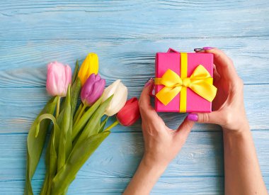 Kadın elleri bir hediye kutusu, ahşap bir arka planda bir buket lale tutuyor.