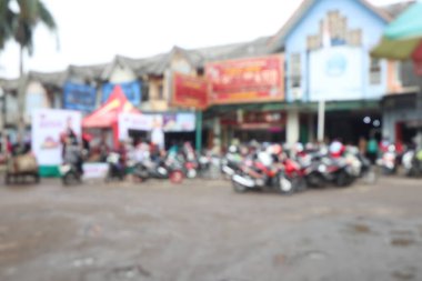 Defocused view of street market atmosphere with people, motorcycles, and shops.