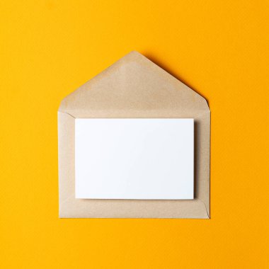 Kahverengi Kraft kağıt zarf, içinde beyaz bir kart var. Saf sarı bir arka plana yerleştirilmiş..