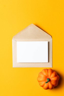 Üzerinde beyaz bir kart olan kahverengi Kraft zarfı, parlak turuncu arka planda küçük dekoratif balkabaklarıyla çevrili..