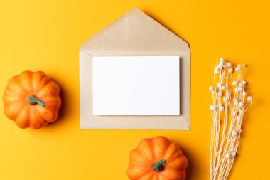 Üzerinde beyaz bir kart olan kahverengi Kraft zarfı, parlak turuncu arka planda küçük dekoratif balkabaklarıyla çevrili..