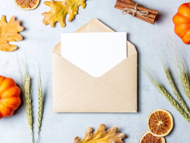 Kahverengi Kraft zarfının içinde sonbahar dekorasyonlarıyla çevrili beyaz bir kart var..