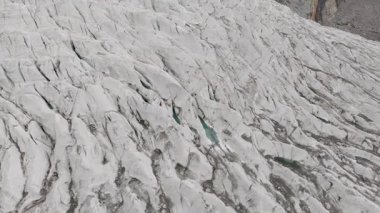 Aerial view of a glacier in Pakistan, showcasing the rugged beauty of its crevasses and turquoise meltwater pools.