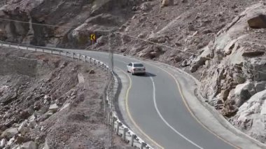 Aerial view of a car navigating a winding mountain road in Pakistan, highlighting the rugged terrain and engineering marvels.