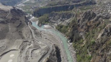 Aerial view of a serene river flowing through a rugged mountain valley in Pakistan, highlighting the natural beauty and sparse human habitation.