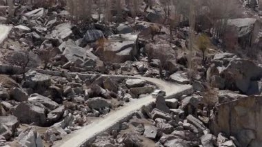 Aerial view of a white SUV navigating a winding dirt road through a rugged mountainous landscape in Pakistan.