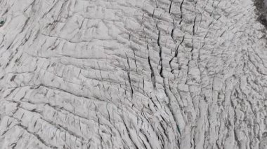 Aerial view of a vast glacier in a remote mountainous region, highlighting the intricate patterns of crevasses and ice formations.