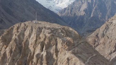Aerial view of a remote mountain peak in Pakistan, featuring a winding road and snow-capped peaks.