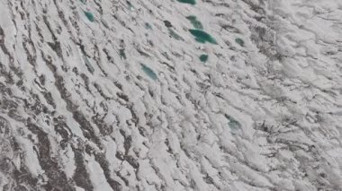 Aerial view of a glacier in Pakistan, showcasing turquoise meltwater ponds and rugged terrain.