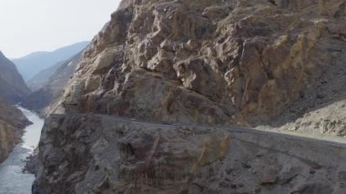Aerial view of a winding road through a rugged canyon in Pakistan, highlighting the dramatic landscape and flowing river below.