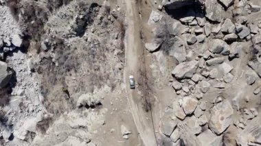 Aerial view of a rugged landscape in Pakistan, featuring a white car navigating a rocky path.