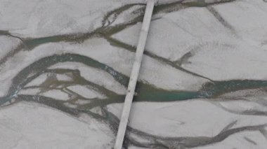 Gün ortasında açık gökyüzünün altında çekilen, karla kaplı kumların arasından akan kıvrılan bir nehrin hava görüntüsü..