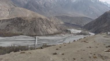 Pakistan 'daki ücra bir vadinin havadan görünüşü, engebeli dağlar ve dolambaçlı bir nehri geçen yalnız bir köprü..