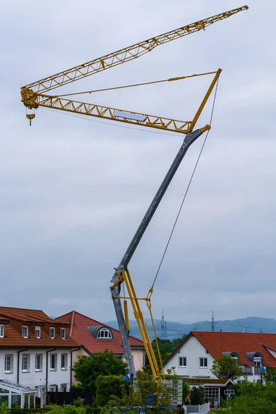 Crane in zigzag shape over red roofs of houses, sky clouds in background