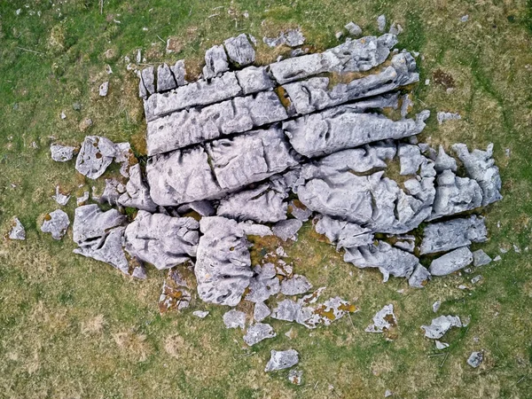 Havadan bakıldığında, yemyeşil çimlerle çevrili, doğal dokuları ve desenleri vurgulayan yıpranmış kayalardan oluşan bir küme görülüyor..