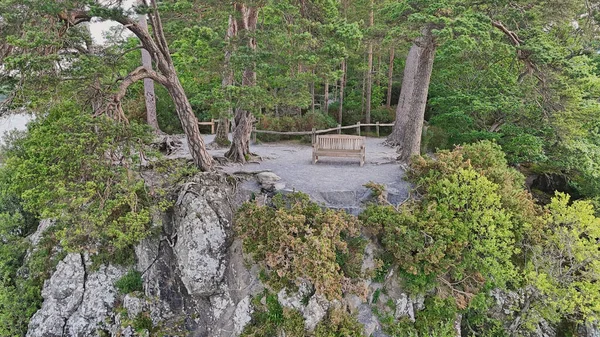 Ağaçların arasına kurulmuş, manzaraya bakan kayalık bir çıkıntının üzerine kurulmuş sakin bir bank manzarası rahatlama ve yansıma için mükemmel. Keşiş Kayalığı, Derwen Suyu