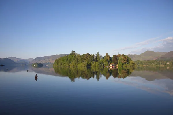 Derwen gölü, berrak mavi gökyüzünün altında yemyeşil ağaçları olan güzel bir adayı yansıtır..