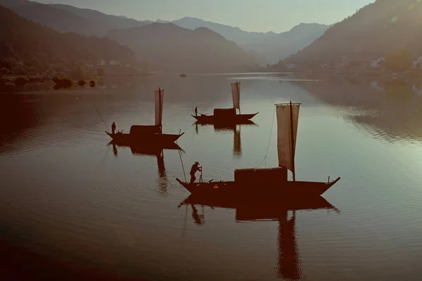 Üç geleneksel tekne sakin sularda süzülüyor, alacakaranlıkta dağlık bir gölün yumuşak ışığına karşı..