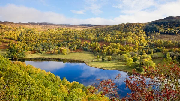 Canlı bir sonbahar sahnesi sergileniyor, sakin bir göl sergileniyor, gür ormanlar ve yuvarlanan tepeler arasında gökyüzünü yansıtıyor, güzel bir manzara..