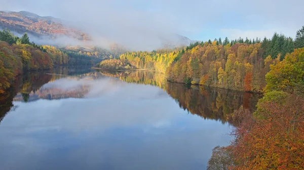 Sakin bir göl, çevreleyen orman ve dağların canlı sonbahar renklerini yansıtarak çarpıcı bir doğal manzara yaratır..