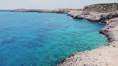 Mavi göl ve Kıbrıs 'ın kayalık kıyılarının hava aracı görüntüsü. Turkuaz Akdeniz suyu ve doğal uçurumları olan deniz manzaralı bir yer. Akdeniz, dalgalar ve uçurumlar