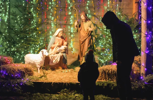 Father and son are watching the Christmas scene. Christmas Manger scene with figures including Jesus, Mary, Joseph, sheep and magi. Soft focus