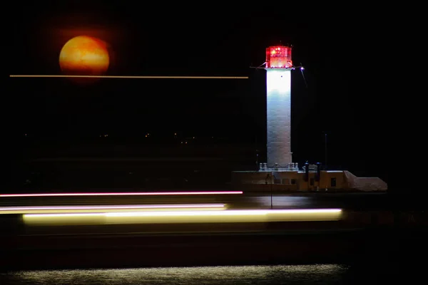 Vorontsov vuurtoren nacht tegen de stijging van de grote rode maan. Oude witte baken vuurtoren lantaarn in de Zwarte Zee haven van Odessa, Oekraïne. Lange blootstelling. — Stockfoto