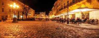 Gece şehrinin eski sokaklarında sokak kafesi. Eski şehir pazar meydanında Lviv şehir ışıklı gece insanlar kafede masalarda oturan. uzun pozlama