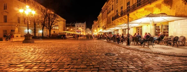 Gece şehrinin eski sokaklarında sokak kafesi. Eski şehir pazar meydanında Lviv şehir ışıklı gece insanlar kafede masalarda oturan. uzun pozlama